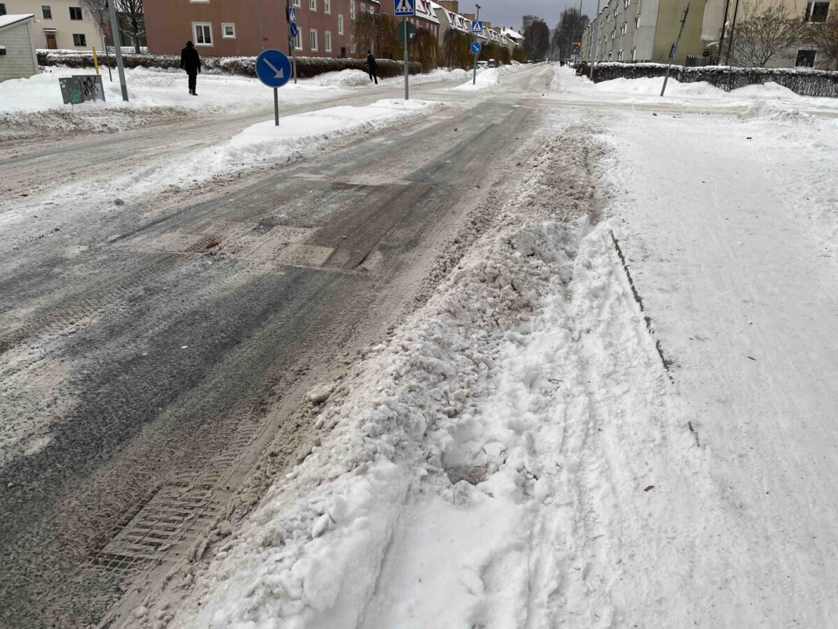 Snö täcker längsgående kantsten vid ramp för cykelbana ner på körbanan.
