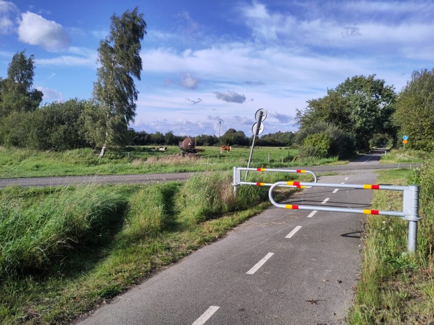 Dubbla bommar på ena sidan, enkel bom på andra sidan. Vägen som korsar är en lågtrafikerad grusväg på landsbygden. Cykelvägen är en regional uppmärkt cykelled.